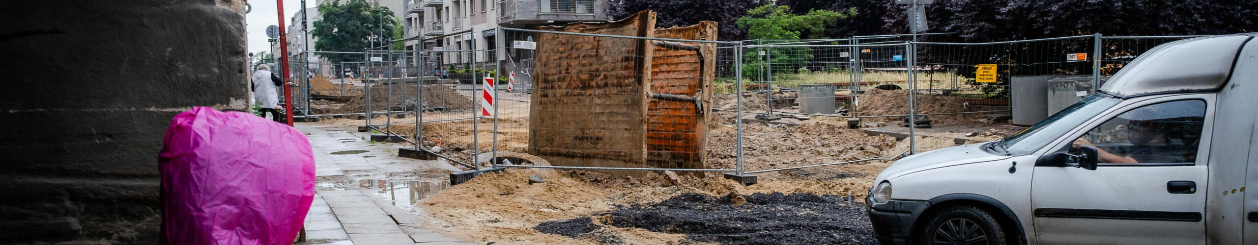 Dziecko w przeciwdeszczowym płaszczu patrzące się na rozkopaną ulicę