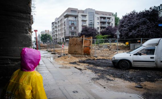 Dziecko w przeciwdeszczowym płaszczu patrzące się na rozkopaną ulicę